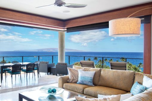Stylish coastal living room opens to a sea-view balcony with a beige sofa, glass coffee table, wicker chairs, and a ceiling fan, bright and airy.