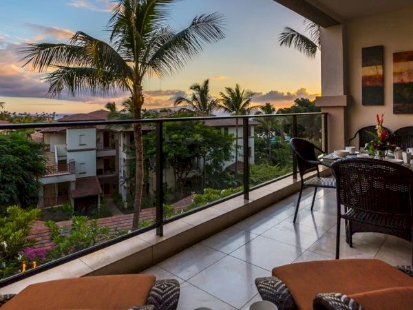 Balcony view at sunset with palm trees, tropical resort vibes, and a table set for two overlooking a lush landscape and distant sunset.