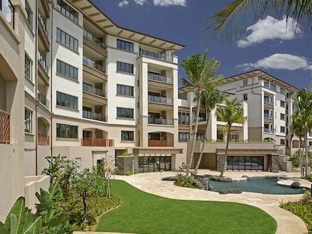 A modern apartment complex with multiple white buildings, a central courtyard, palm trees, and a swimming pool area, sunny tropical vibes.
