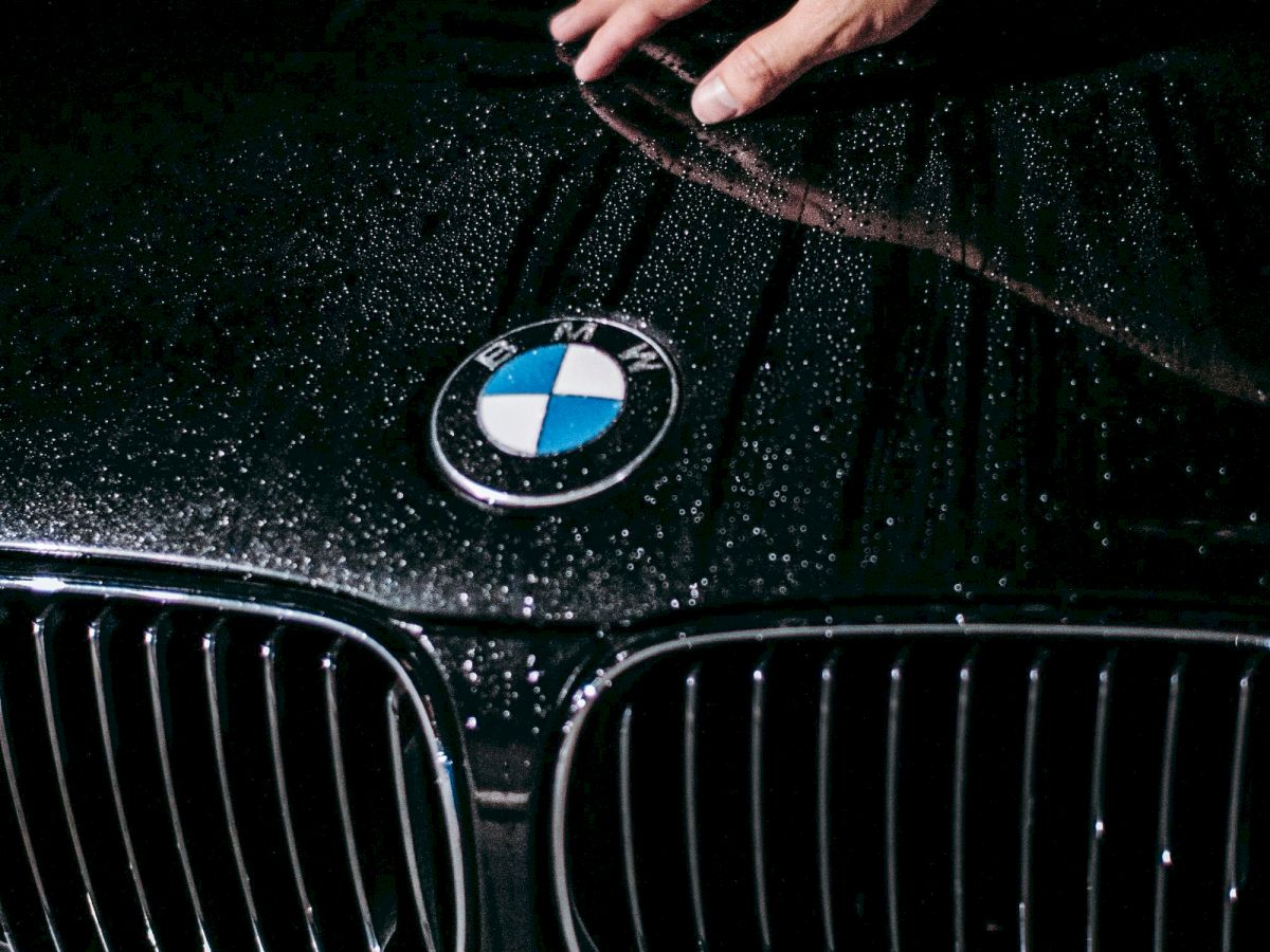 A hand wipes a wet, black BMW hood with a water spray shimmering on the surface.