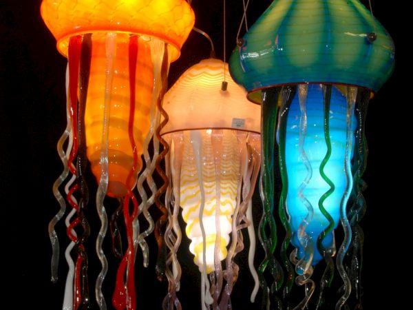 Colorful jellyfish-shaped lanterns glow against black, each with dangling tendrils and bright hues of orange, white, and blue.