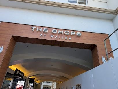 The Shops at Wailea entrance, showing a wooden archway and curved walkway into the shopping area.