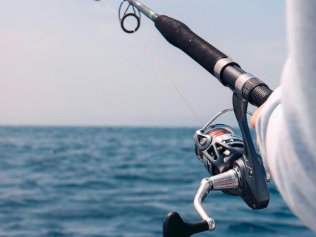 A person fishing off a boat, holding a spinning rod over the water.