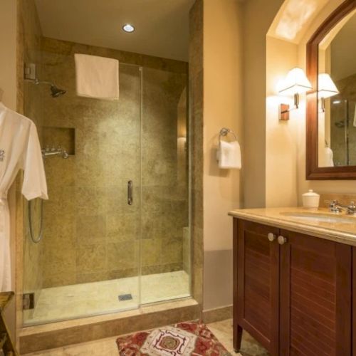 A bathroom with a glass-enclosed shower, beige tile, a wooden vanity, and a mirror; soft lighting and a towel hanging near the sink.